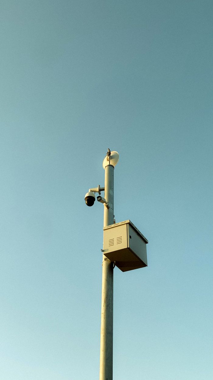 A streetlight pole with surveillance and safety cameras against a clear blue sky.