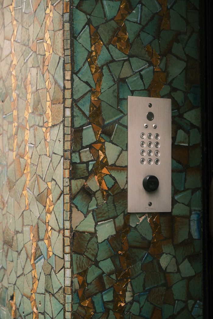 Close-up of a modern intercom on a decorative mosaic wall in an urban setting.