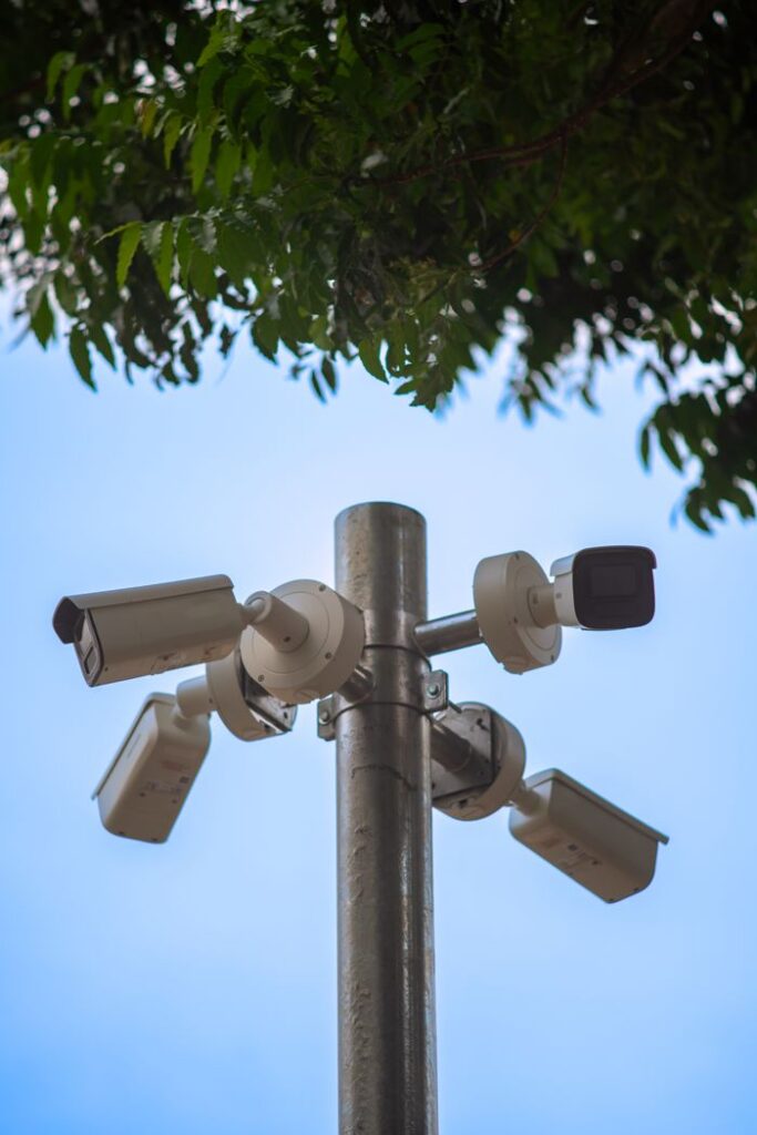 Multiple security cameras mounted on a metal pole under a tree, ensuring public safety.